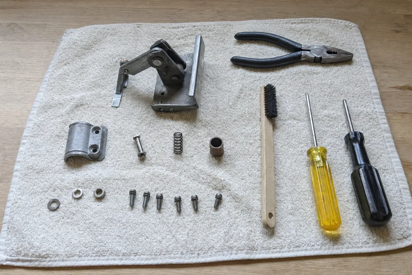 A cast hinge mechanism with its sprung arm and pivot laid out on a cloth beside a saddle clamp, a compression spring, a bronze bush, washers, screws and hand tools